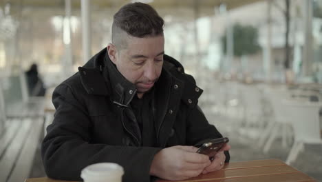 Focused-man-in-black-coat-using-smartphone-in-cafe